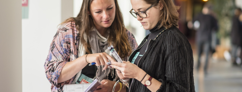 Zwei Frauen stehen auf deinem Gang und schauen gemeinsam in einen Plan