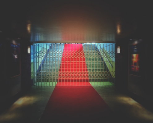 Eisengitter verschließt den Zugang zu einer mit rotem Teppich bedeckten Treppe.